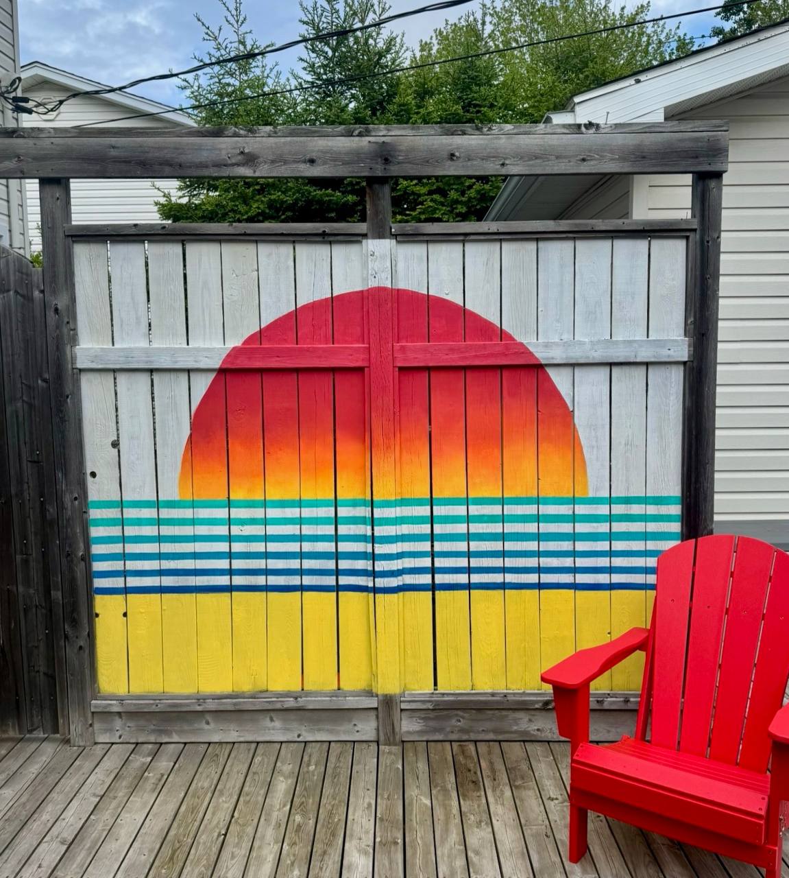 Bright sunset mural painted on a backyard fence with a red chair
